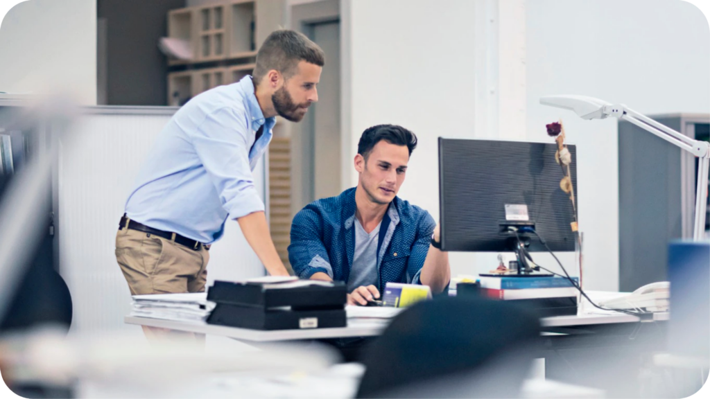 Photo of two men working behind a computer.